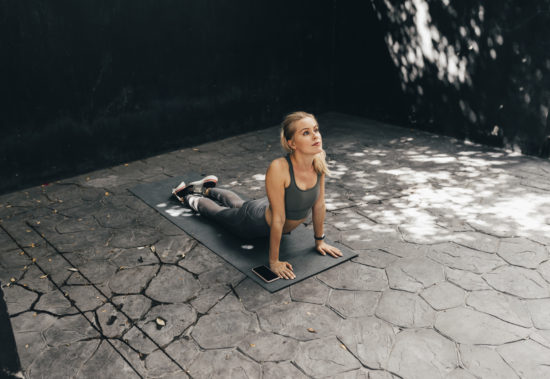 An attractive young woman doing exercises on a yoga mat by following an online app on her smartphone.